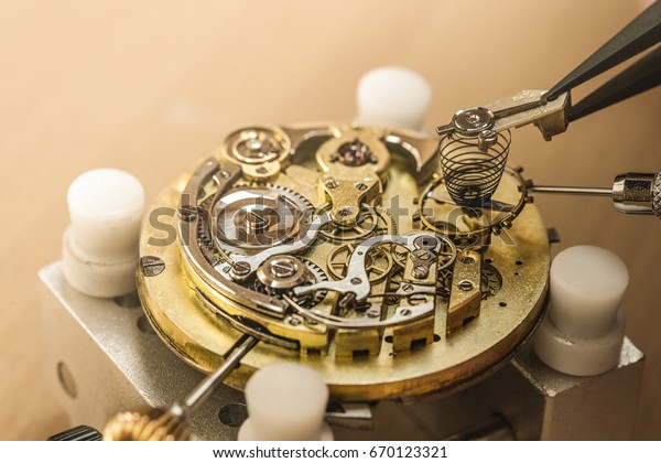 Cropped close up of a repairman putting a spring\
into mechanical vintage pocket watch he is repairing. Clockworks at\
the workshop machinery mechanism retro old styled hobby occupation\
fix concept