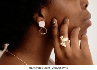 Cropped close up side view of unrecognizable Black woman wearing matching designer earrings and golden ring on white background