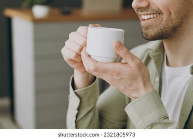 Cropped close up side view young smiling happy caucasian cool man wears shirt casual clothes drink tea sitting alone at table in coffee shop cafe restaurant indoors rest relax during free time inside