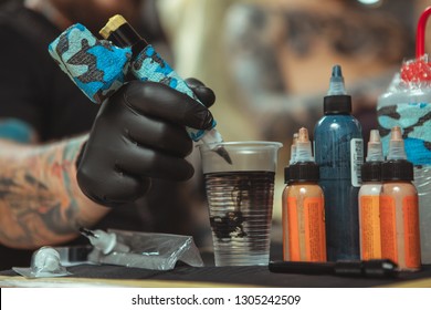 Cropped Close Up Of Tattoo Ink Spreading In Glass Of Water, Tattoo Artist Cleaning His Tattoo Machine In A Glass Of Water, While Working. Selective Focus On Tattoo Machine Of A Tattooist, Copy Space