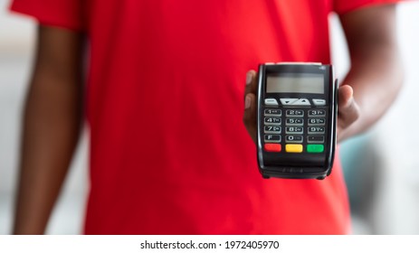 Cropped Close Up View Of African American Man In Red Uniform Holding POS Machine, Selective Focus On Payment Terminal, Blurred Background. Digital Contactless Transaction