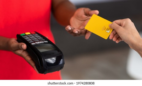 Cropped Close Up View Of African American Man In Red Uniform Holding Point Of Sale Machine In Hand, Woman Giving Credit Card, Selective Focus On Payment Terminal. Digital Contactless Transaction