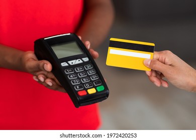 Cropped Close Up View Of Female Client Paying With Credit Card On Payment Terminal, Black Man In Red Uniform Holding Pos Machine In Hand. Digital Contactless Cashless Transaction Concept