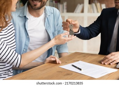 Cropped close up view happy couple receiving keys from new own property, finish meeting in real estate agency lead by realtor in formal suit. Bank mortgage for young family, selling, renting concept