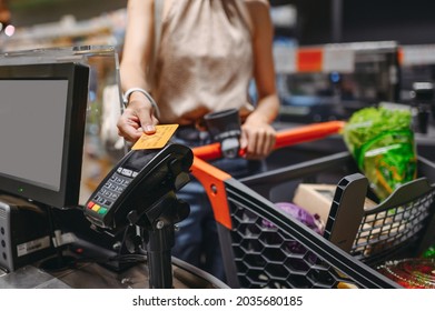 Cropped close up woman hand shopping at supermaket put credit card to wireless modern bank payment terminal process acquire payments near cashier checkout with cart inside store. Purchasing concept - Shutterstock ID 2035680185