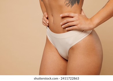 Cropped close up young nice lady woman with slim body perfect skin wearing nude lingerie stand akimbo put hand hold waist isolated on plain pastel light beige background. Lifestyle diet fit concept
