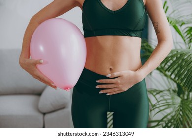 Cropped close up young strong sporty athletic fitness trainer instructor woman wear green tracksuit training hold balloon near belly do exercises at home gym indoor. Workout sport motivation concept - Powered by Shutterstock