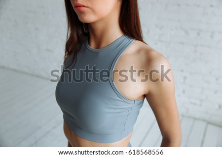 cropped closeup of the body of a fit woman wearing a sports bra, showing slim belly and press in diet fitness and concepts of healthy lifestyle, isolated on white brick background