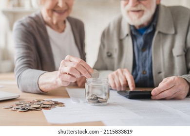 Cropped closeup focused image. Savings concept. Caucasian old elderly senior grandparents couple husband wife spouses putting coin into moneybox, economy for nest egg, pension, mortgage loan at home