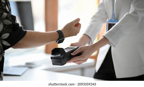 Cropped, close-up image of a man using his modern digital wristwatch paying his shopping. NFC technology, cashless society, Social distance.