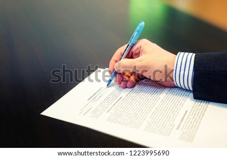Cropped closeup of a man hand filling in Non Disclosure Agreement (NDA). Reading and signing business concept