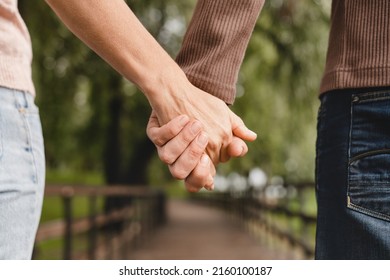 Cropped closeup photo of a mature heterosexual couple holding hands together while walking on a date in park outdoors.