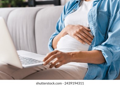 Cropped closeup portrait of a pregnant woman`s belly with laptop searching browsing information about fertility and child care, maternity leave. Future mother, motherhood concept - Powered by Shutterstock