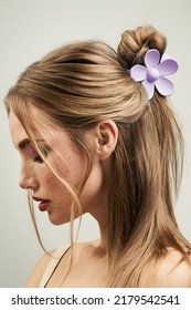 Cropped close-up shot of a blonde girl with a claw clip in her hair. Portrait of a young woman with a violet flower hair claw clip on a pastel background. Side view.           - Shutterstock ID 2179542541