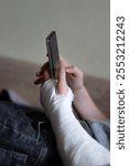 Cropped close-up shot of a boy with a broken arm wrapped in a white plaster cast. Teenager uses phone, 