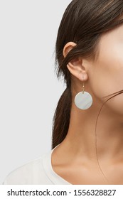Cropped close-up shot of a brunette woman in an ivory white top and with a golden hook earring with dangling nacre disc.  - Shutterstock ID 1556328827