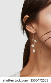 Cropped close-up shot of a brunette woman in an ivory white top and with a hook earring made as a curly golden brunch with leaves, gem flower and shimmering pearls.   - Shutterstock ID 1556472101