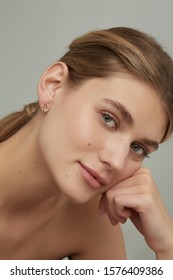 Cropped Close-up Shot Of A Charming Woman With A Stud Earring Made As A Golden Flower Crown With Sparkling Crystals, Pink Gems And Jeweller's Enamel. The Lady's Blonde Hair Is Gathered In A Knot.