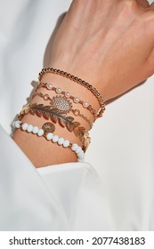 Cropped close-up shot of a female wrist with a golden ethnic bracelets set with various decorative embellishments. The lady is dressed in a white shirt. The photo is made on the white background.     