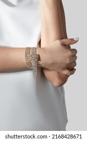 Cropped close-up shot of a woman with a gold rhinestone bracelet with a buckle. The woman in a white blouse is wearing a rhinestone bracelet on a light background. Front view.