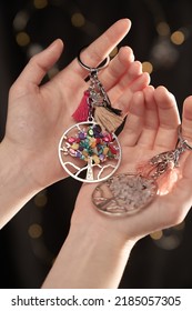 Cropped close-up shot of woman's hands holding two Tree of Life keychains decorated with colored stones, tassels and an owl pendant. A girl is holding two metal keychains with bokeh background.