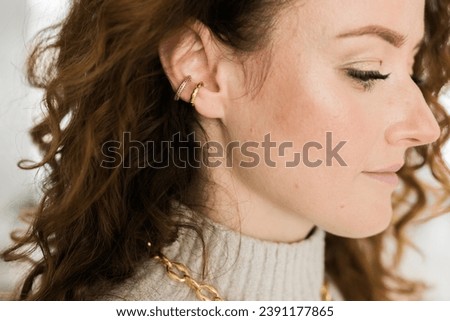 Cropped close-up shot of a young woman with two asymmetrical golden ear cuffs. Female with golden ear cuffs, side view.