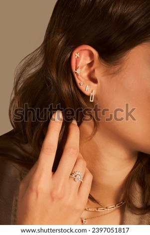 Cropped close-up shot of a young woman with asymmetrical gold ear cuffs. Female with gold ear cuffs, side view