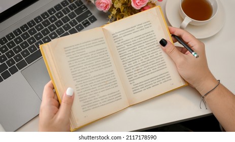Cropped, closeup top view image of a teenager female reading an inspiration novel book at her desk.