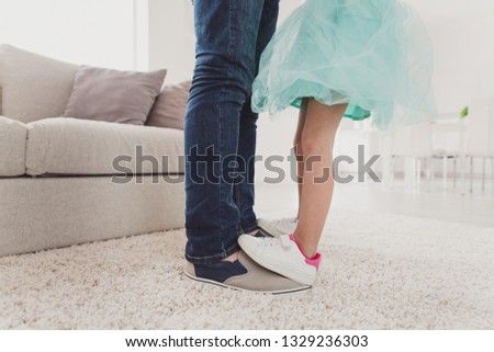 Cropped close-up view of nice two pairs of legs exquisite fashionable trendy stylish elegant pre-teen girl dancing on dad's feet trust support in modern light white interior room carpet