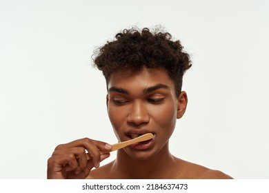 Cropped Of Concentrated Black Guy Brushing His Teeth With Toothpaste. Young Slim Brunette Curly Man. Dental Care And Hygiene. Isolated On White Background. Studio Shoot. Copy Space