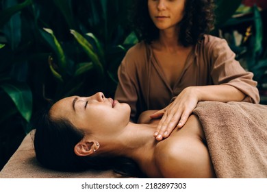 Cropped cosmetologist doing dermatology procedure with perfect body skin and massage to Asian client spending seans at nature, woman relaxing and recreating during beauty therapy on dayspa