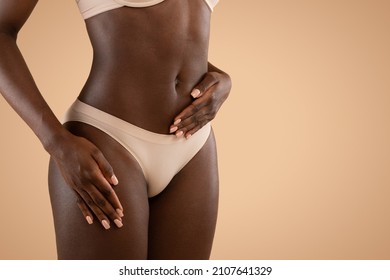Cropped of dark skinned woman in nude underwear holding hand on belly, african american lady got pregnant, waiting for baby, beige studio background, panorama with copy space
