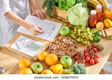 Cropped Dietitian, Nutritionist Or Doctor Standing By Desk Writing About Benefits Of Eating Fresh Fruit And Vegetables