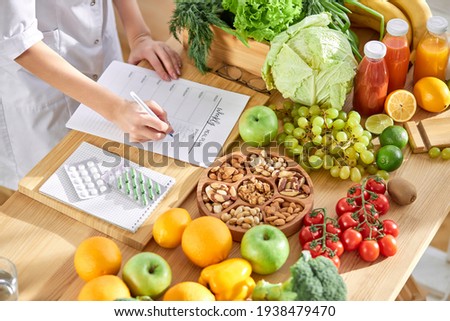 Cropped dietitian, nutritionist or doctor standing by desk writing about benefits of eating fresh fruit and vegetables