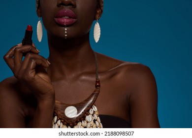 Cropped Of Elegant Black Girl With Lipstick. Obscure Face Of Beautiful Young Woman Wear Traditional African Outfit And Accessories. Female Beauty. Isolated On Blue Background. Studio Shoot. Copy