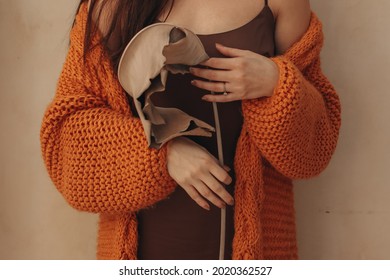 Cropped Female Body In An Orange Knitted Cozy Cardigan Holding A Beige Dry Plant. Autumn Aesthetic