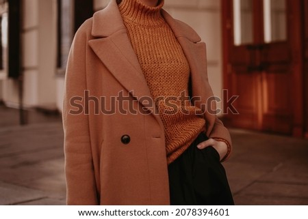 Cropped female figure in a brown cozy warm coat and knitted orange sweater. Street casual winter or autumn fashion.