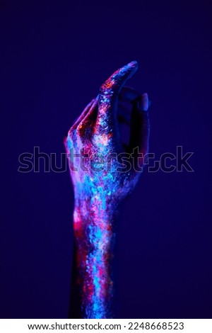 cropped female hands in calm position, painted with fluorescent painting powder. unrecognizable woman raising hands up, on neon light background, copy space. body art concept