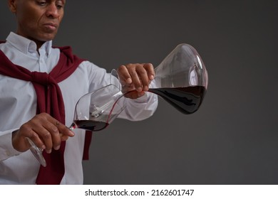 Cropped of focused african american winemaker or sommelier pouring red wine from decanter in glass. Wine tasting. Viticulture and winemaking. Isolated on grey background. Studio shoot. Copy space