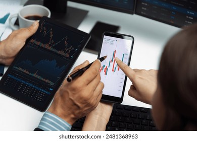 Cropped with focusing on phone with hand pointing with discussing dynamic stock market in two business traders on screens on real time currency rate investment risk data at modern office. Postulate. - Powered by Shutterstock