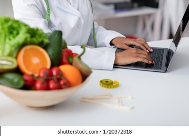 Cropped Of Fresh Fruits And Vegetables Bowl Next To Working Online African Doctor, Dietician Using Laptop