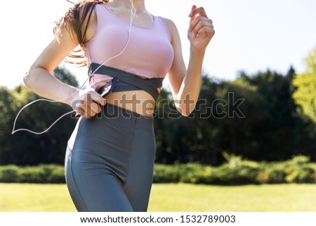 Cropped front view of thin athletic corps of a girl who is running in the park in the sportswear