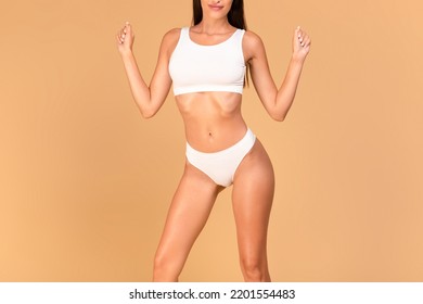 Cropped Frontal View Of Lady With Perfect Body Shape And Flat Tummy Posing On Beige Studio Background, Woman In White Top Bra And Panties