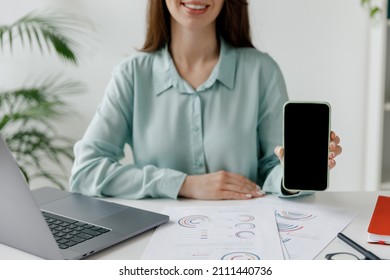 Cropped Fun Young Employee Business Woman In Blue Shirt Use Hold Mobile Cell Phone Blank Screen Workspace Area Sit Work At Desk With Laptop Pc Computer At Office Indoors. Achievement Career Concept.