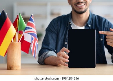 Cropped Of Guy Sitting At Desk With International Flags, Pointing At Digital Tablet With Empty Screen, Recommending Mobile Application For Foreign Language Studying, Educational Online Course, Mockup