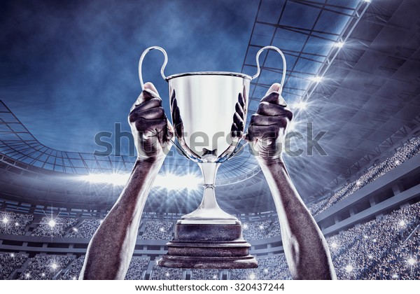 Cropped hand of athlete holding trophy against\
football stadium