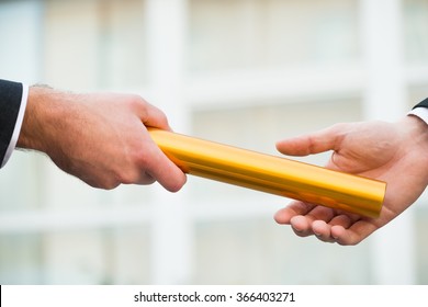 Cropped hand of businessman giving golden relay baton to colleague outdoors