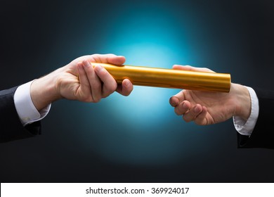 Cropped hand of businessman passing golden relay baton to colleague against blue background
