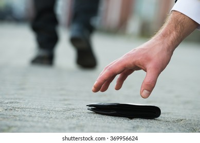 Cropped Hand Of Businessman Picking Up Fallen Wallet On Street