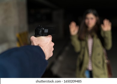 Cropped Hand Of Criminal Pointing Gun At Female Victim Standing In Parking Lot